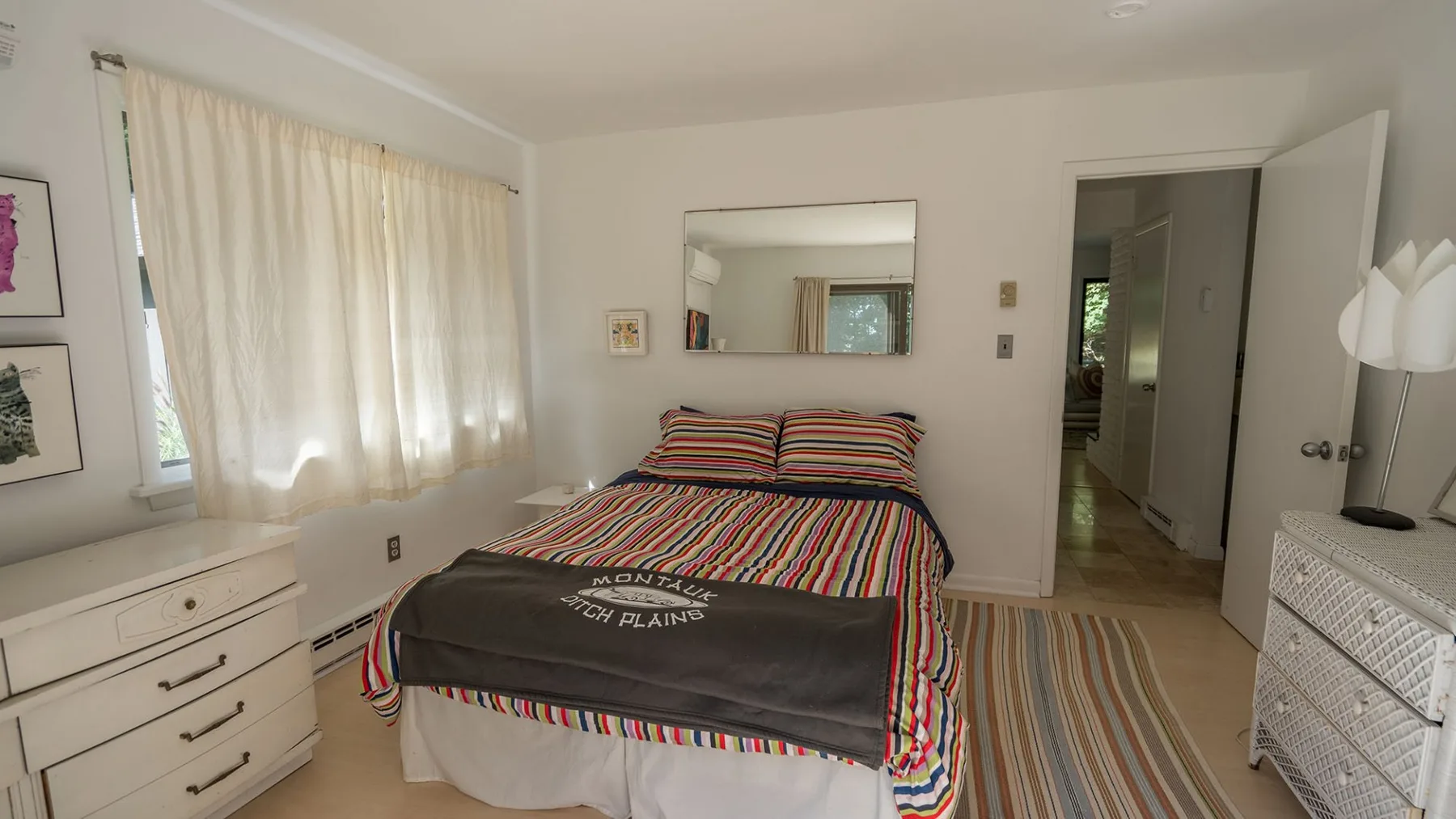 A bedroom with a bed, striped bedding, and a large window with curtains.