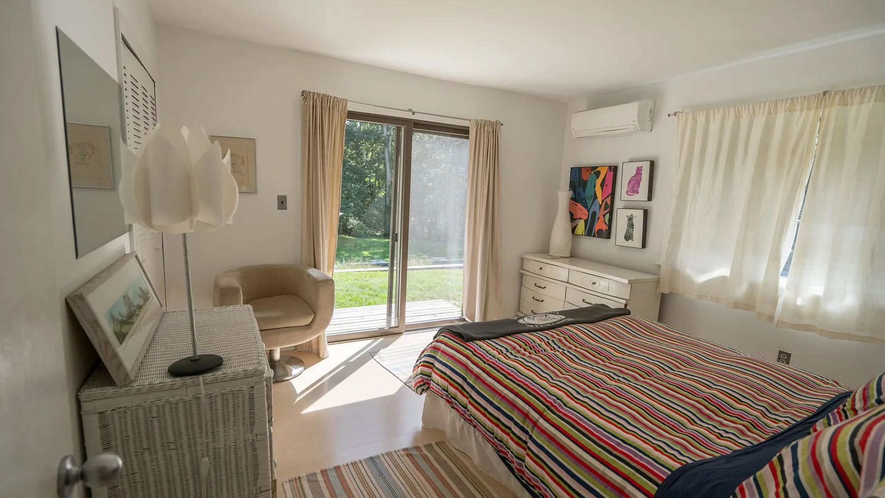 A bedroom with a striped bedspread, a sliding glass door, and a dresser.