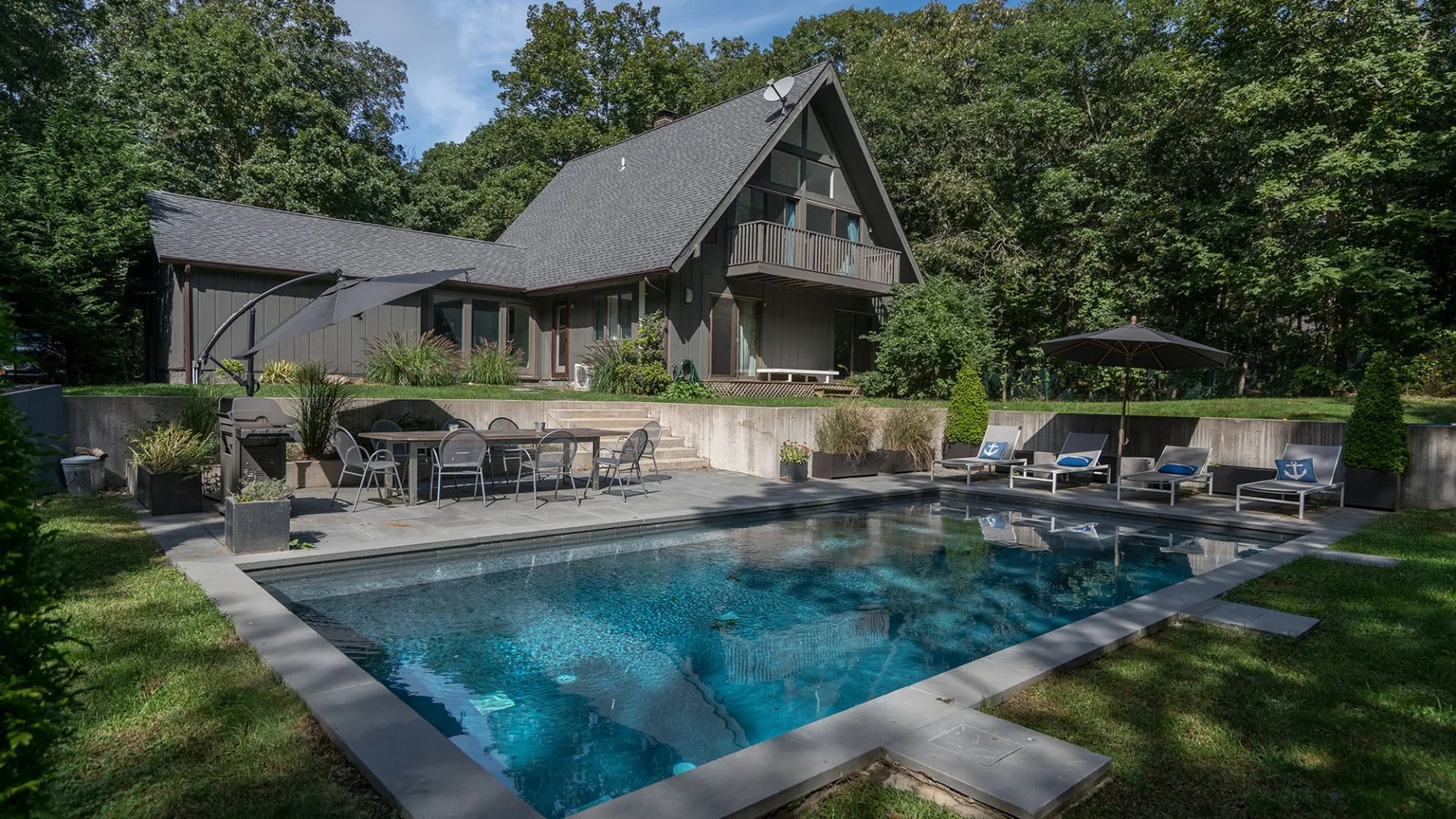 Una piscina está frente a una casa grande rodeada de árboles.