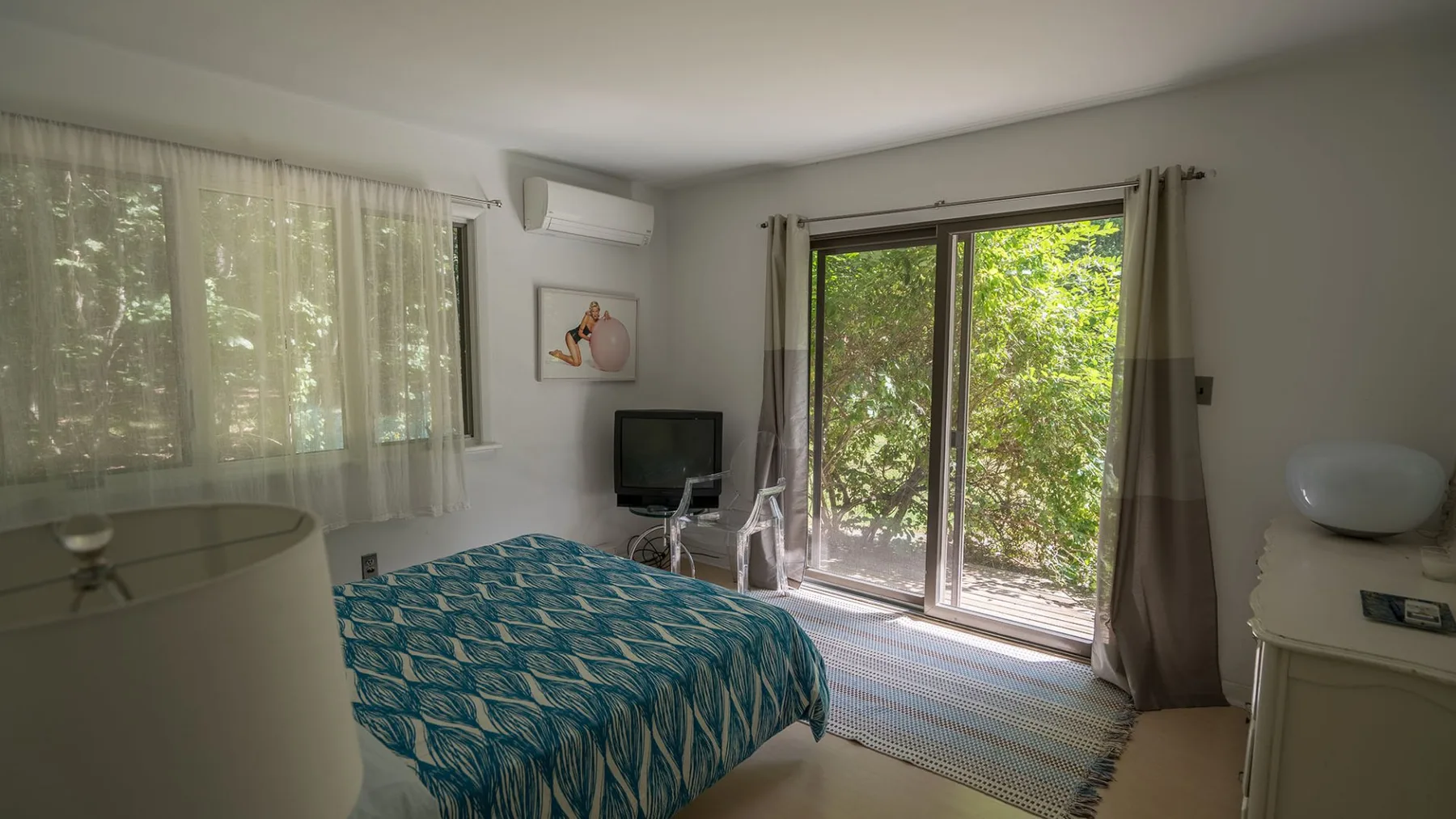 A bedroom with a bed beside glass doors opening onto greenery.
