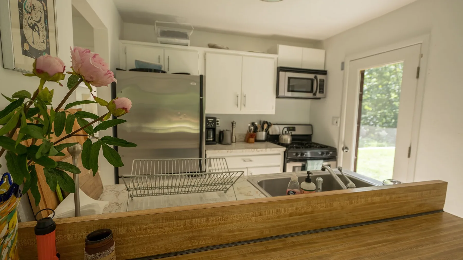 A bright kitchen with white cabinets, stainless steel appliances, and a wooden counter.