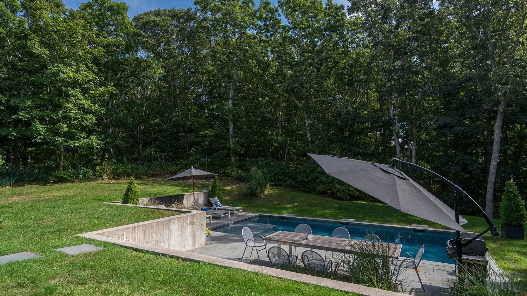 An outdoor swimming pool beside a grassy lawn and surrounding trees.