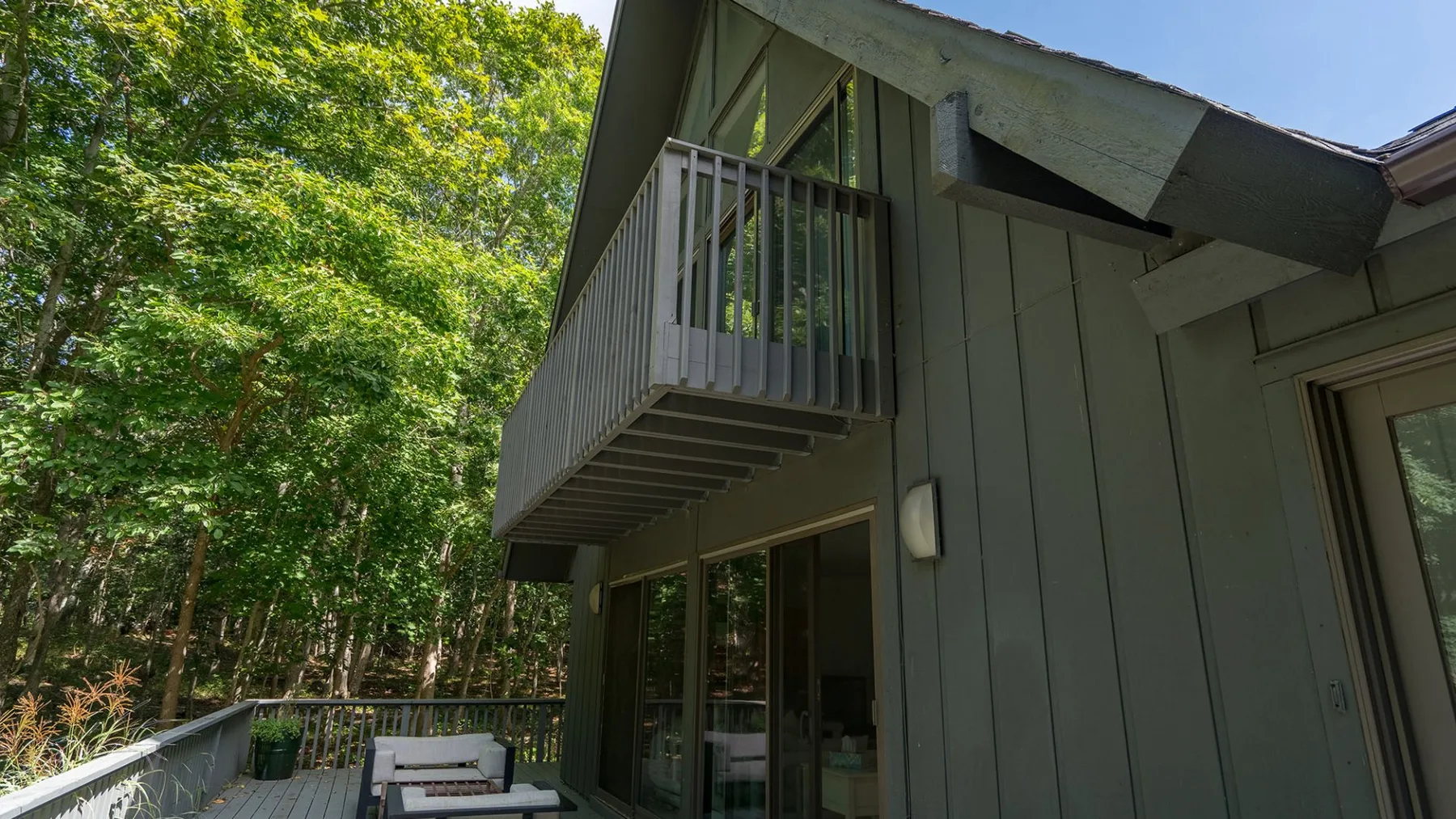 A wooded exterior of a house with a small balcony above a glass door.