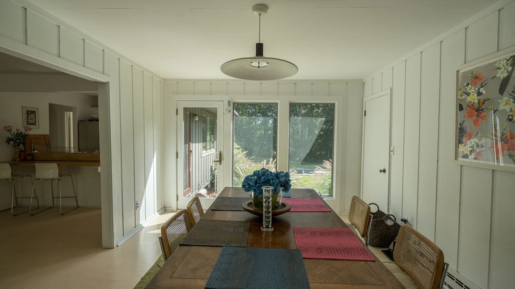 A bright dining area with a long table beside large windows.