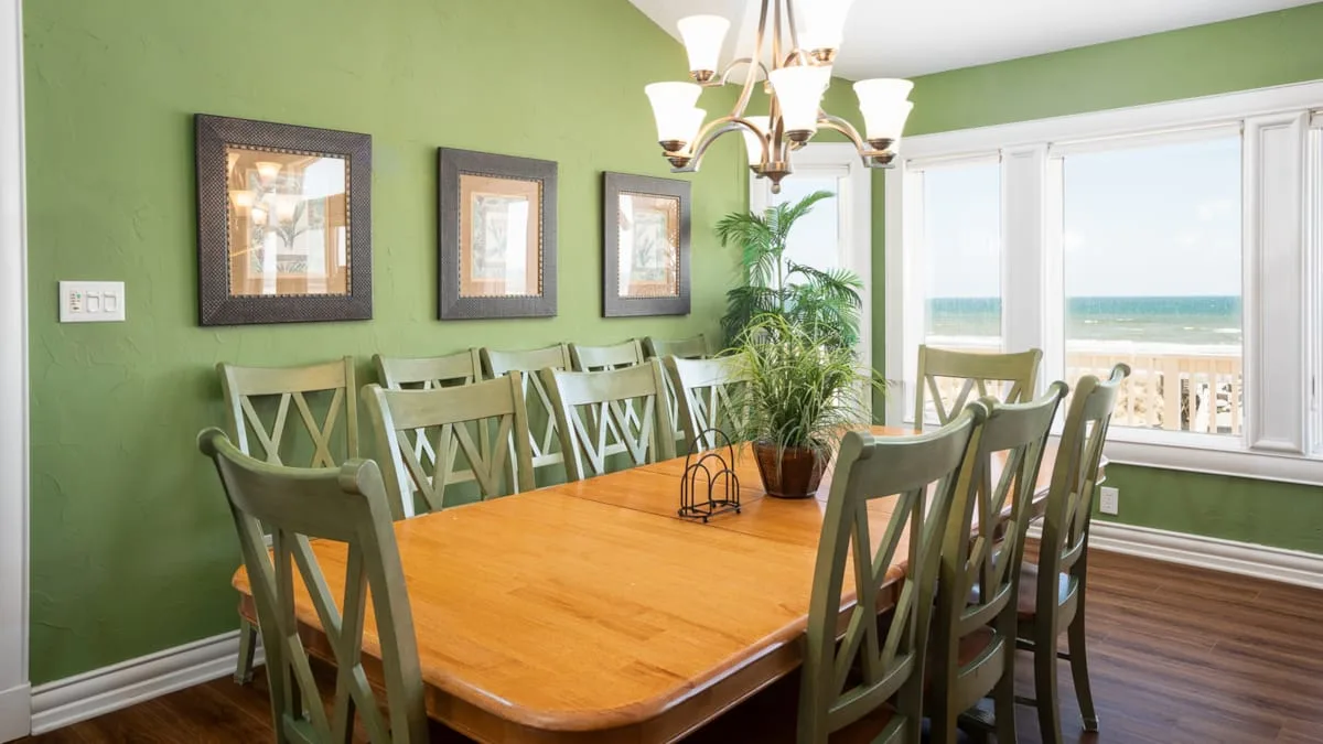 A dining room with a wooden table and green seating beside large windows.
