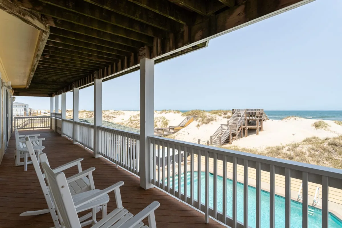 Una terraza de madera cubierta da a una piscina, dunas de arena y el océano.