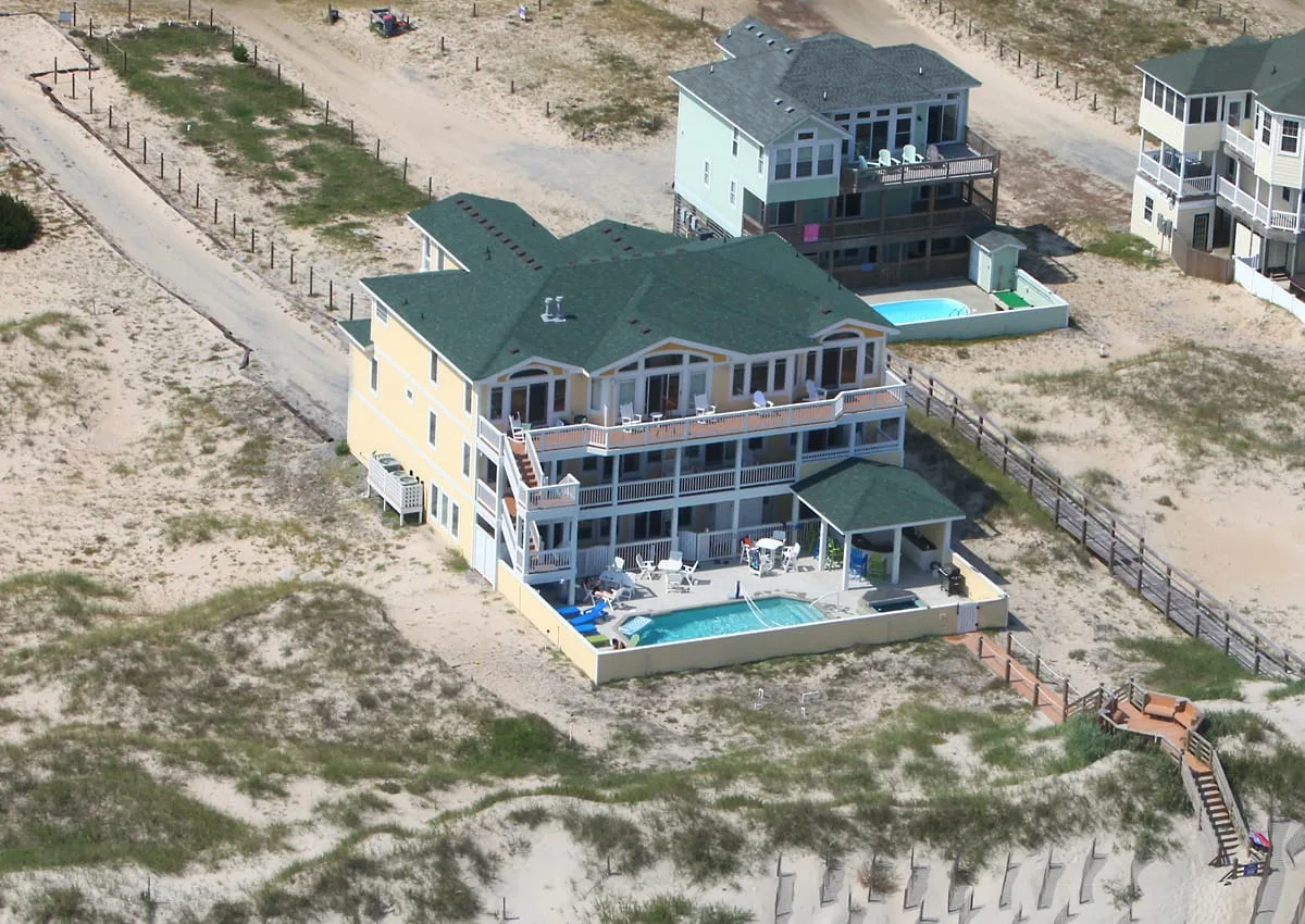 Vista aérea de una gran casa junto a la playa con piscina y terraza.