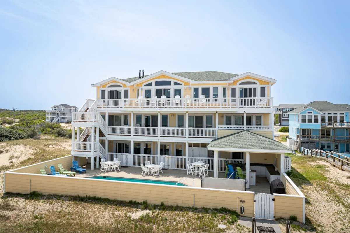 Una gran casa de playa elevada con amplias terrazas se alza entre dunas costeras.