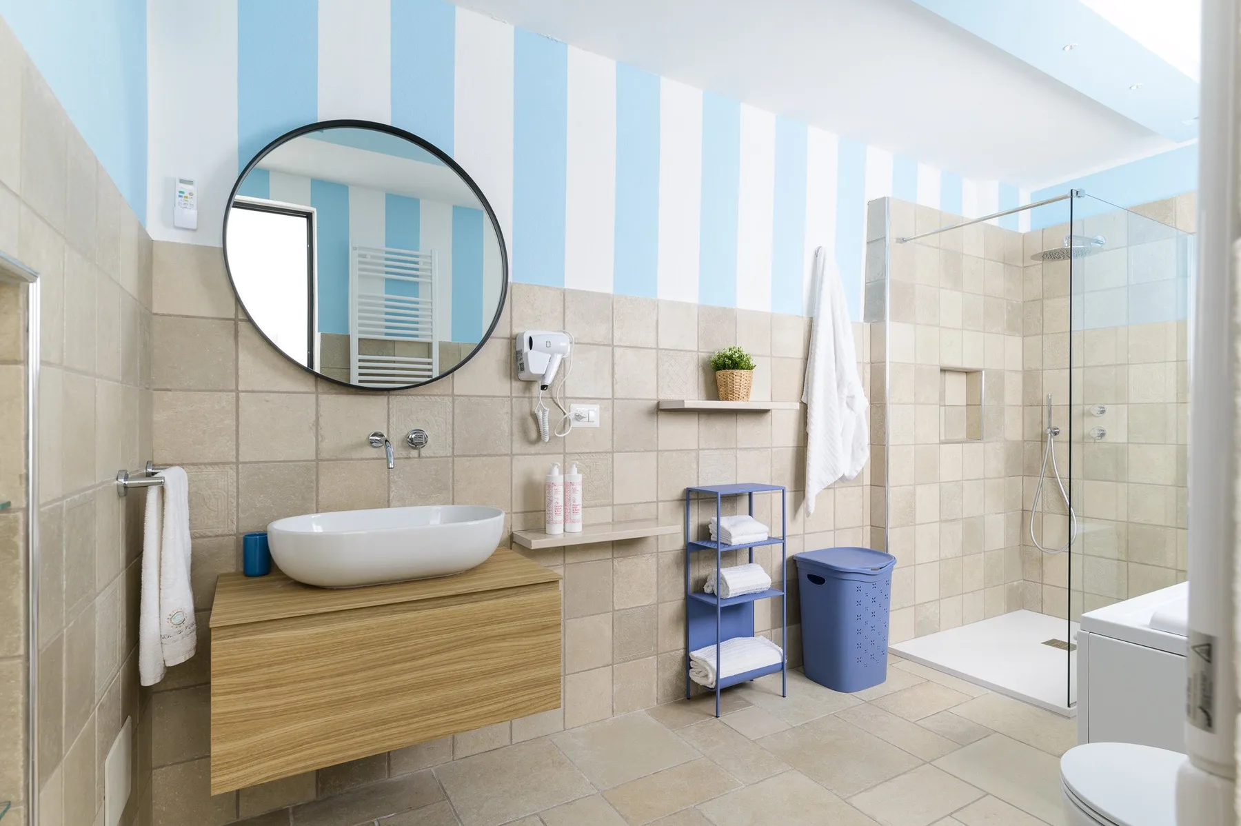 A bright bathroom with a vanity, round mirror, and glass shower.