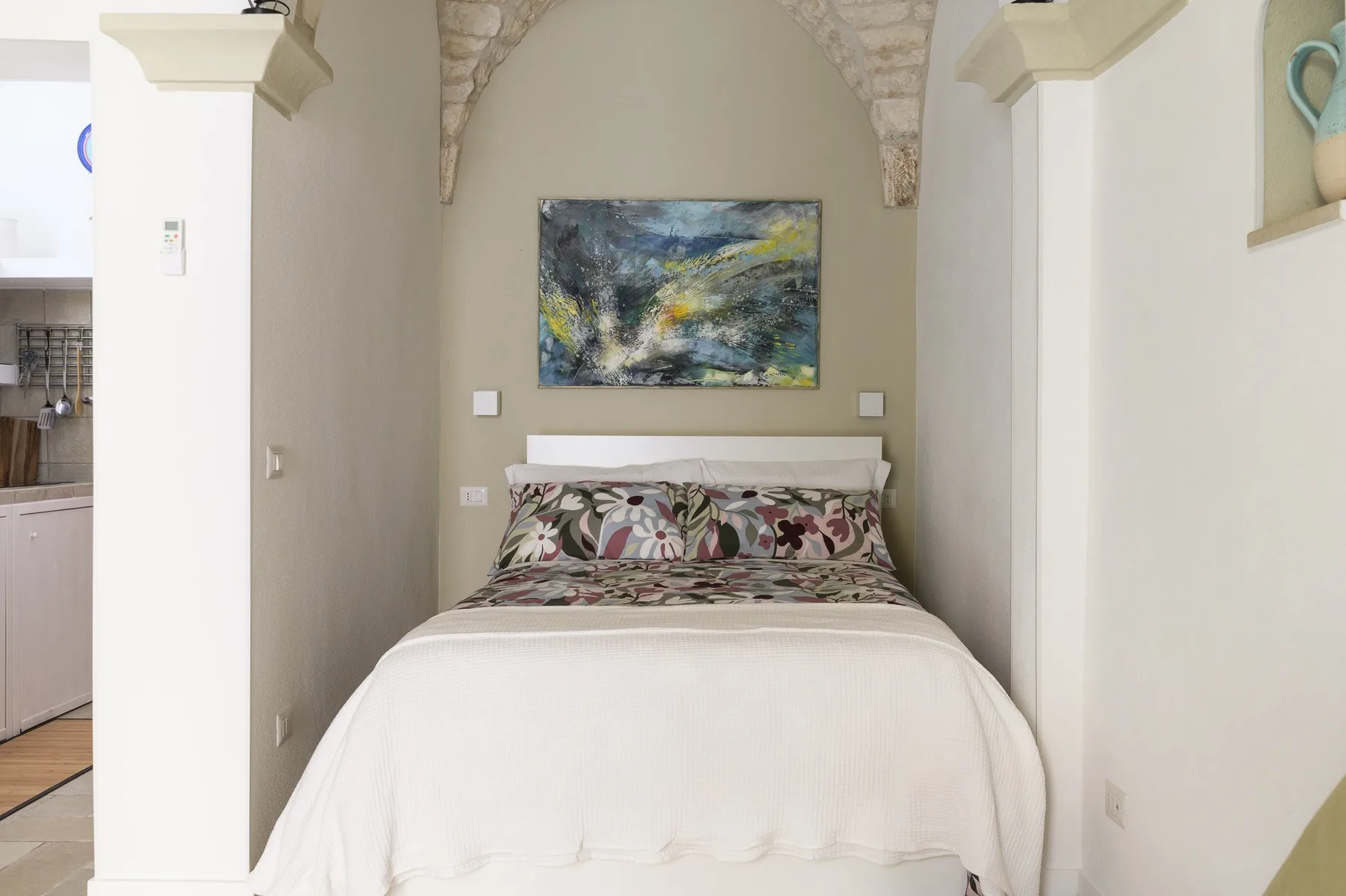 A bedroom with a neatly made bed beneath an arched stone detail.