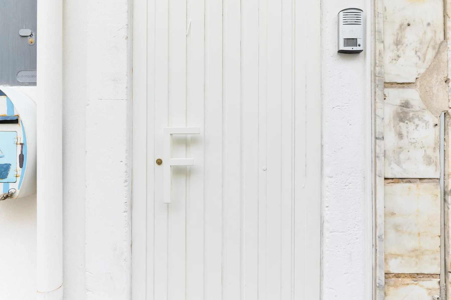 A white entrance door with a small wall-mounted intercom beside it.