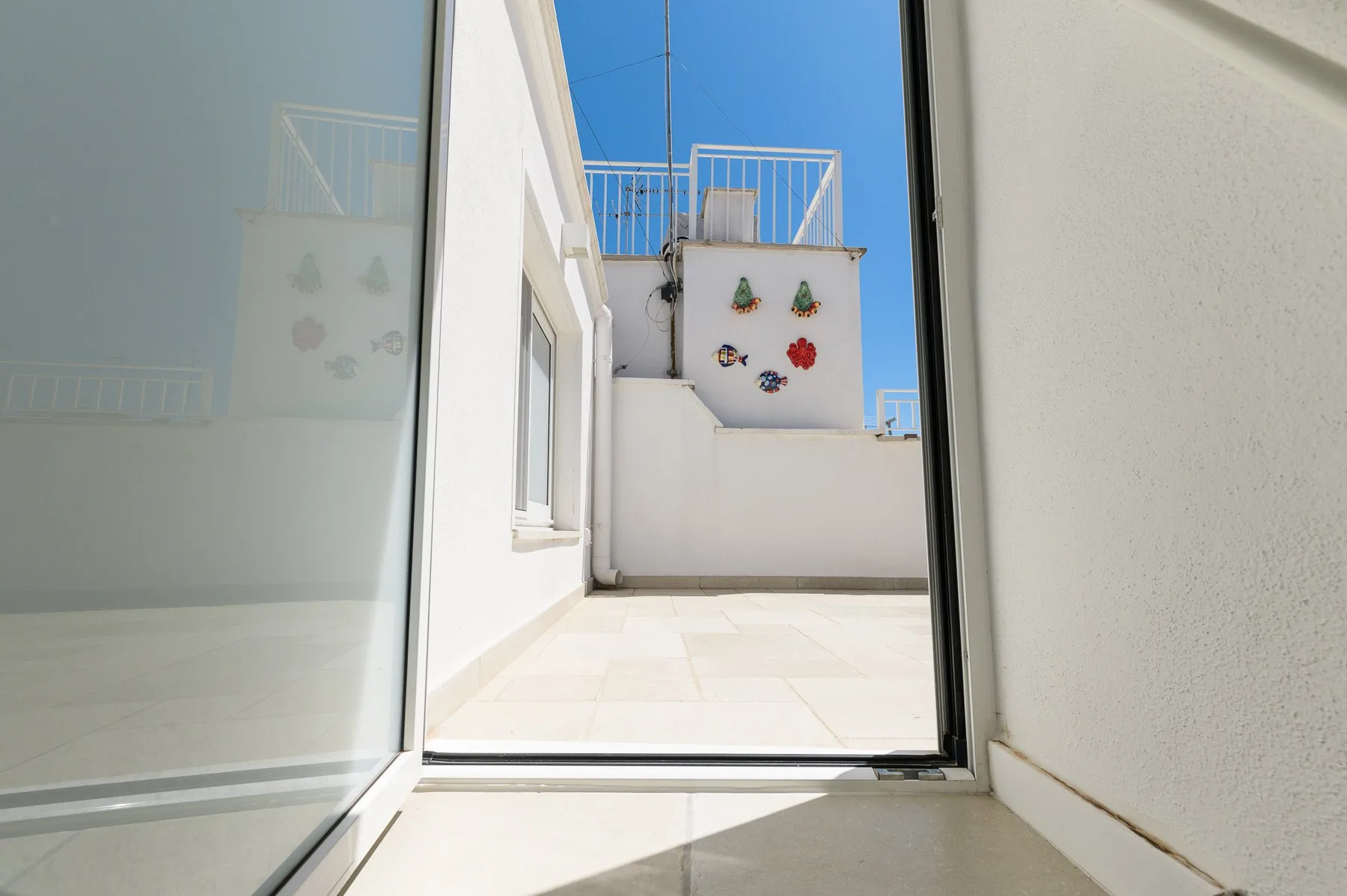 An open glass doorway leads to a bright rooftop terrace with decorative wall tiles.
