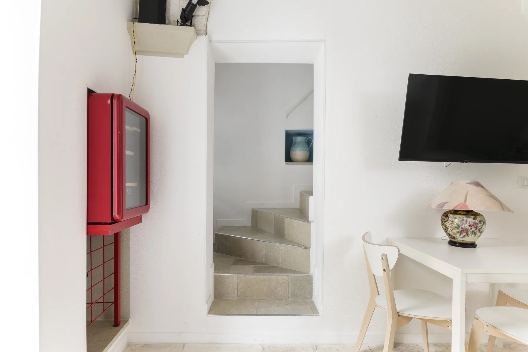 A bright dining area with a table beside a staircase and wall-mounted television.