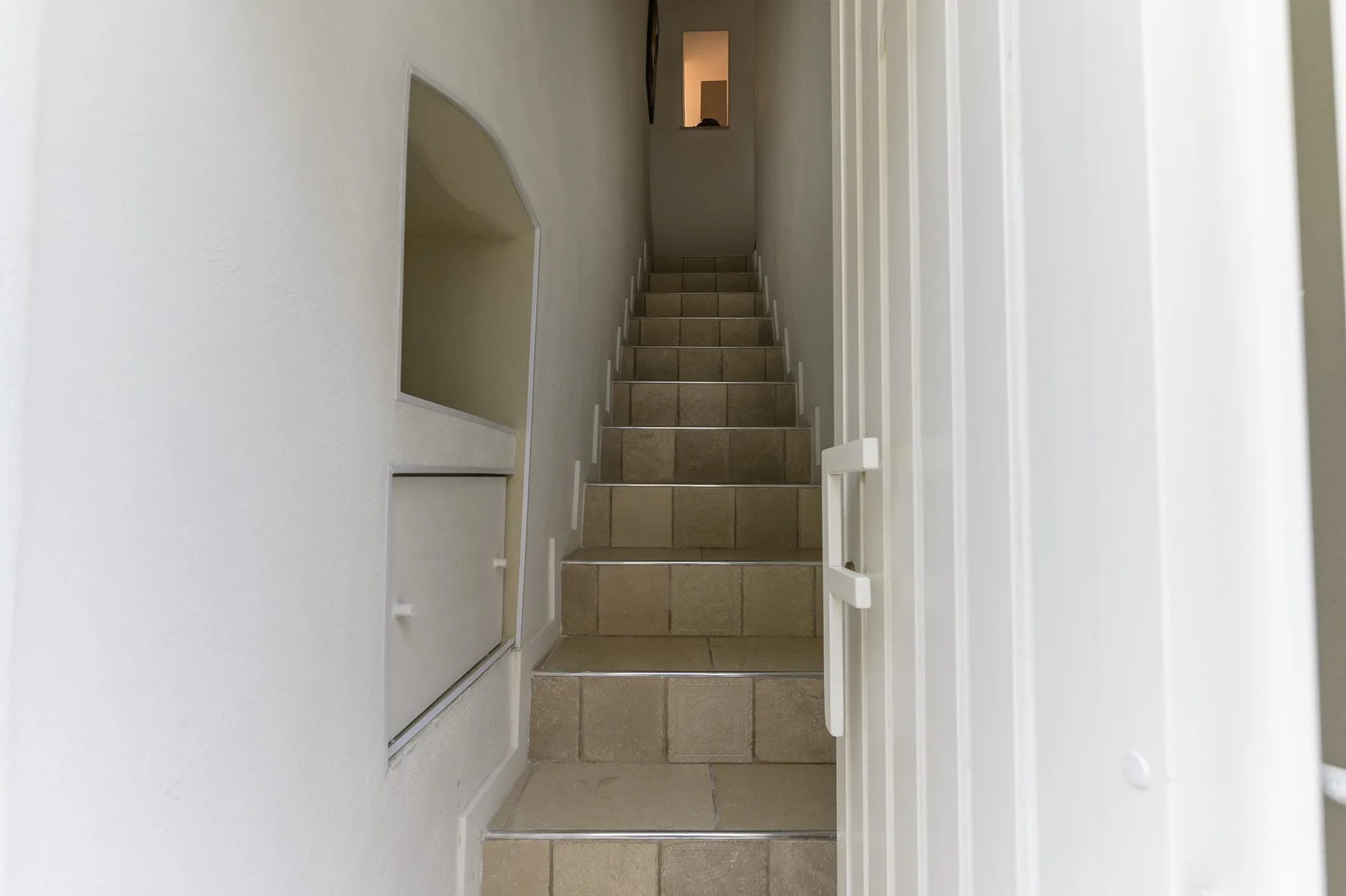 A narrow indoor staircase with tiled steps rises between white walls.