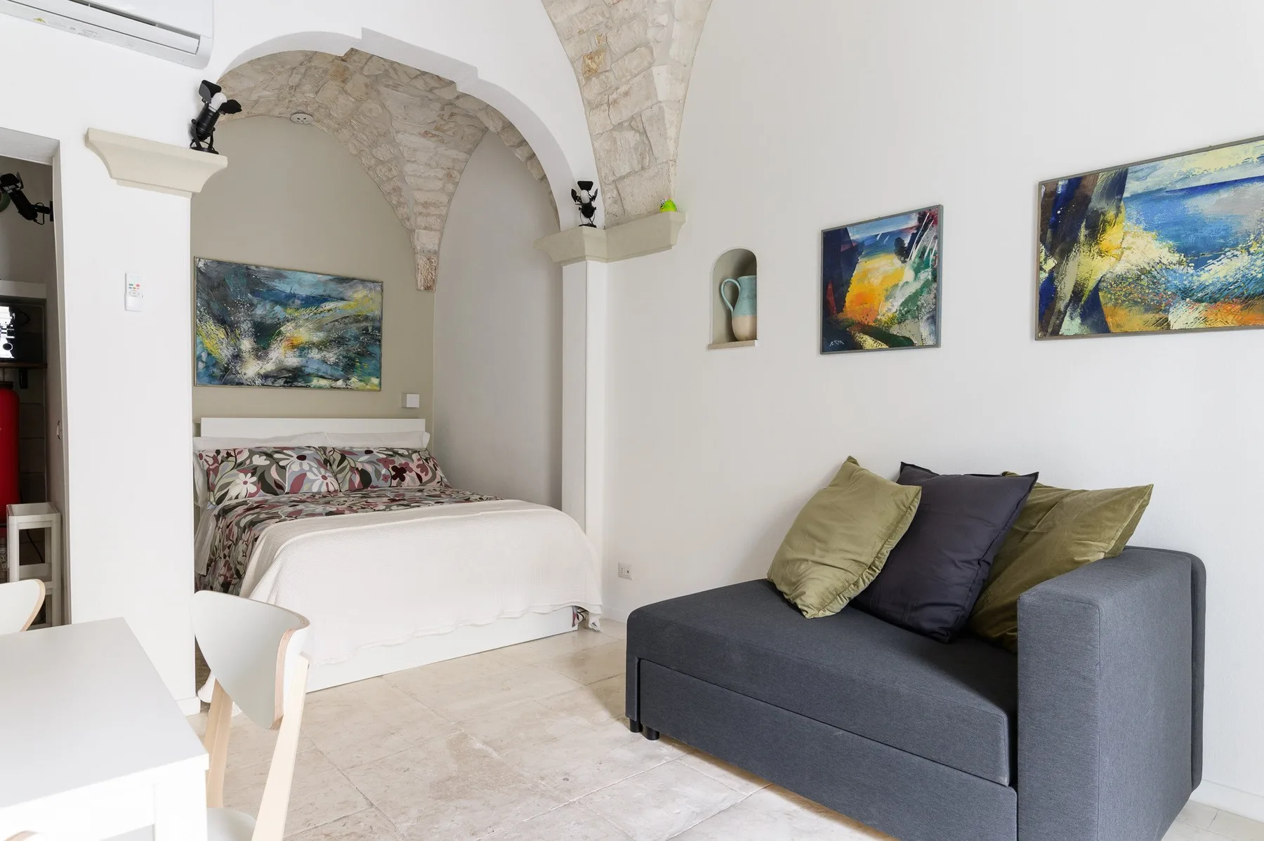 Un dormitorio con una cama y un sofá gris oscuro bajo cuadros coloridos.