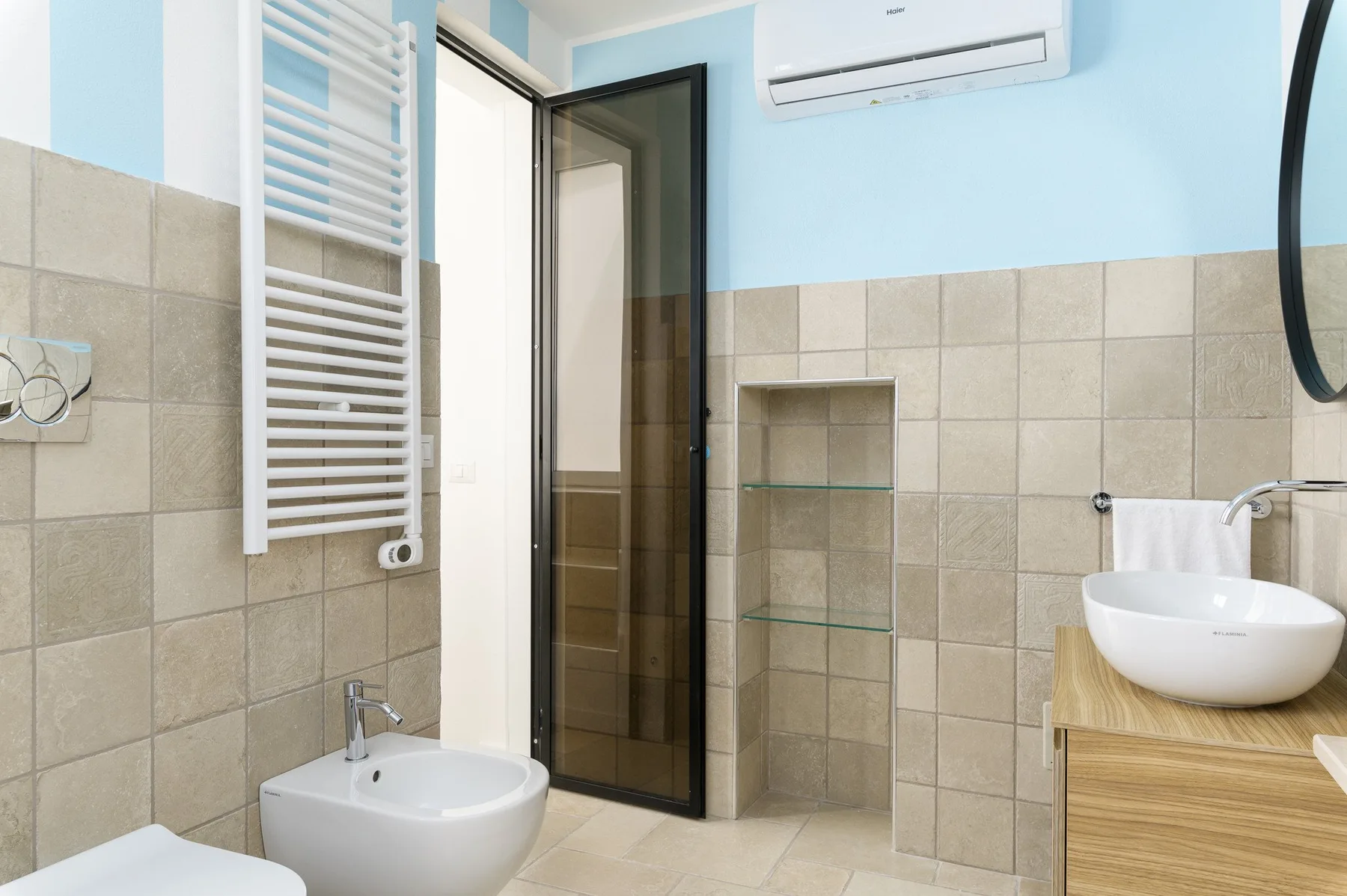 A tiled bathroom with a sink, wall-mounted towel warmer, and open shelving.