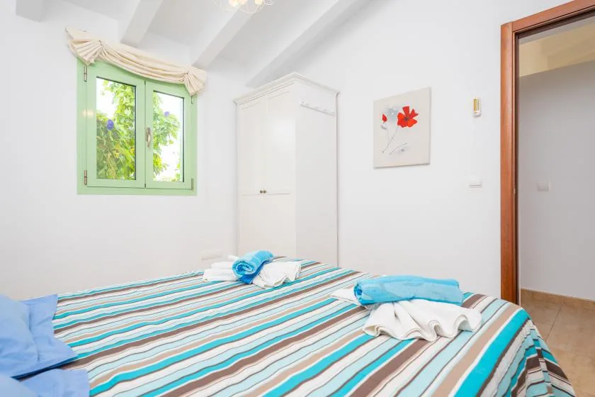 A bedroom with a striped bedspread and a green-framed window.