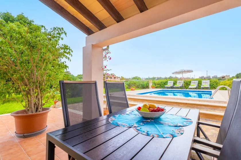A shaded patio dining area overlooks a swimming pool and garden.