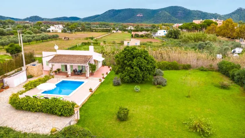 A house and swimming pool sit beside a broad green lawn, with fields and hills beyond.