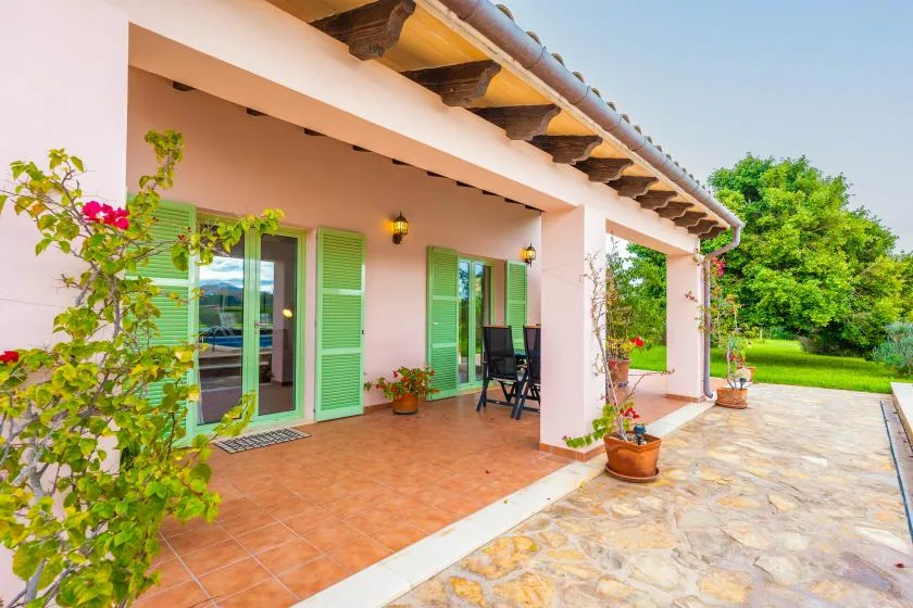 A covered patio with green-shuttered doors opens onto a garden.