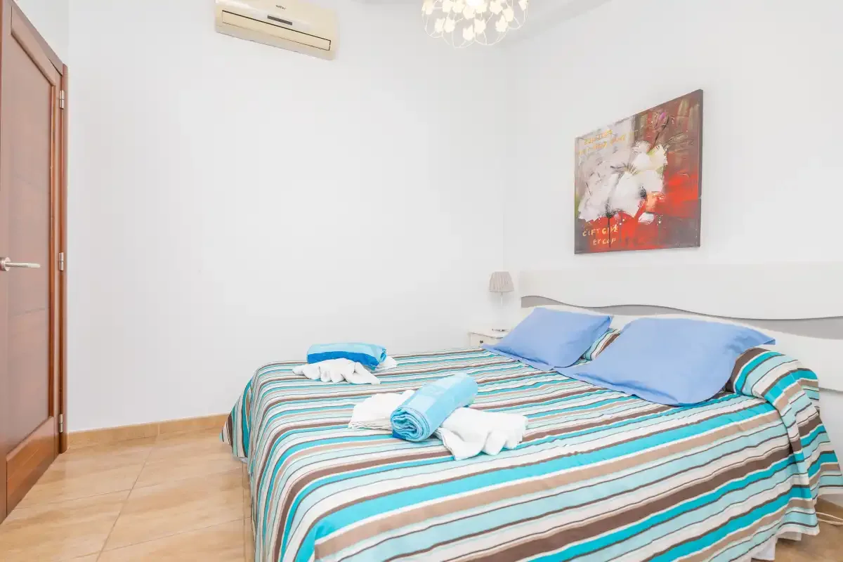 A bedroom with a striped bedspread, blue pillows, and a wall painting.