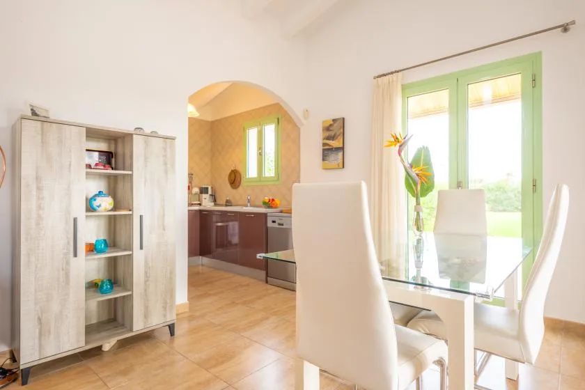 A bright dining area with a glass table beside a green-framed window.