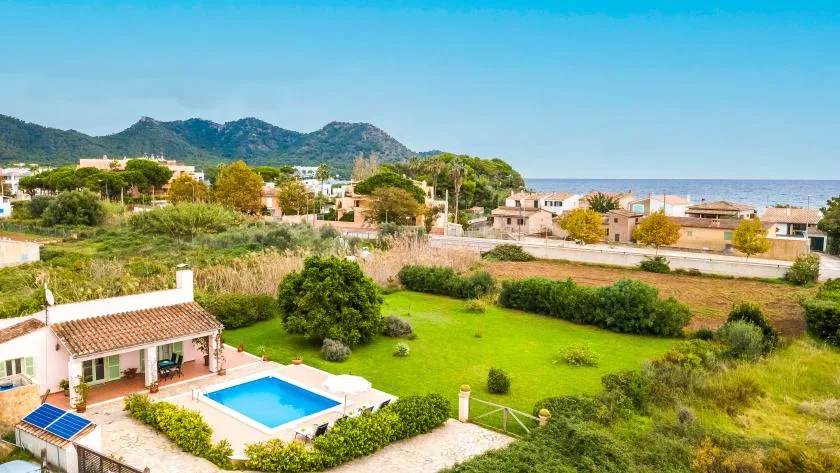 A garden and swimming pool sit beside a small house, with hills and the sea beyond.