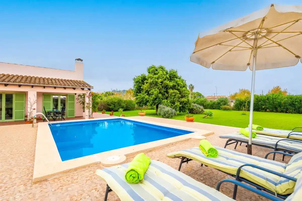 A backyard pool beside a patio with lounge seating and a large umbrella.