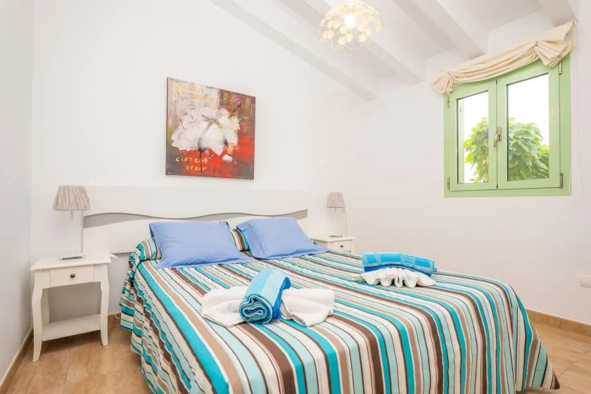A bright bedroom features a bed with striped bedding and a green-framed window.