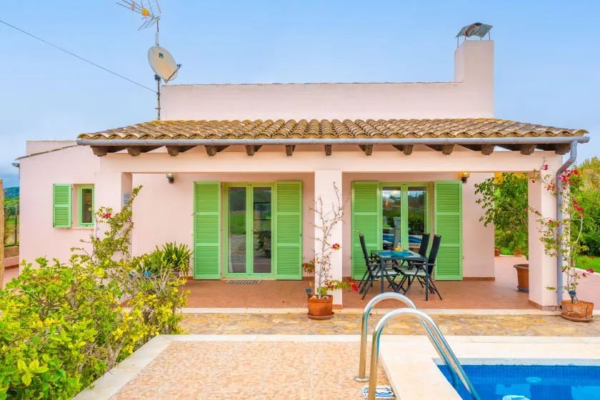 A pink house with green shutters faces a patio and swimming pool.