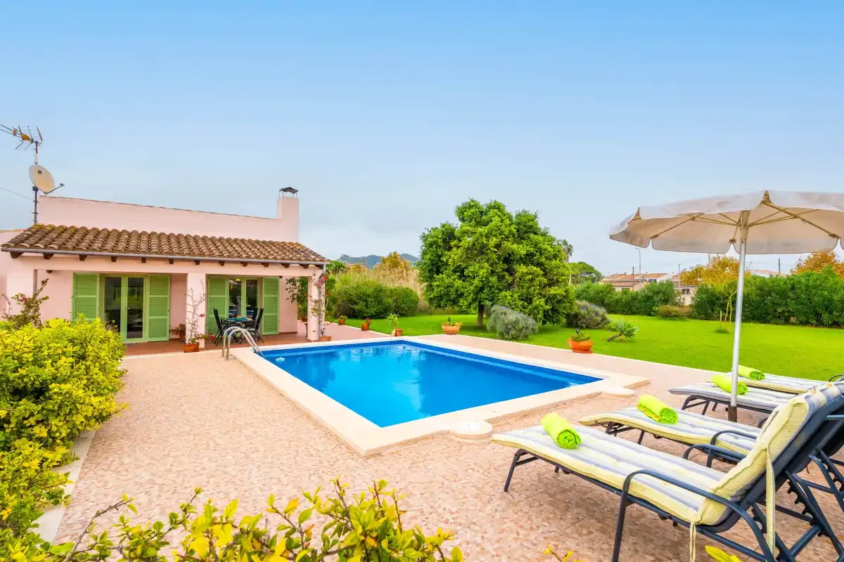 A garden patio with a swimming pool, lounge chairs, and an open umbrella.