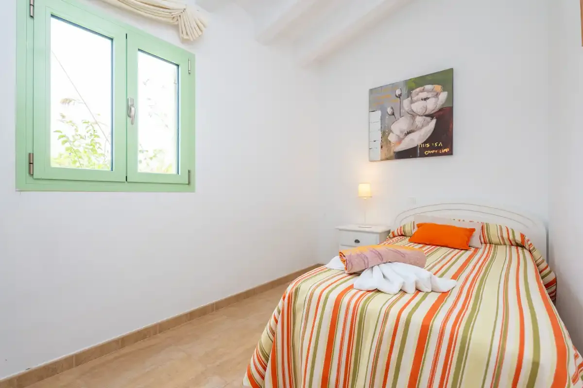 A bedroom with a striped bedspread and a green-framed window.