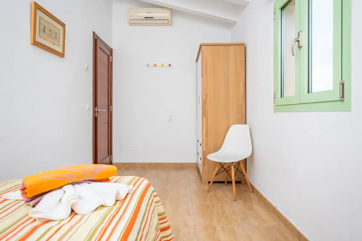 A bedroom with a striped bedspread, a chair, and a green-framed window.