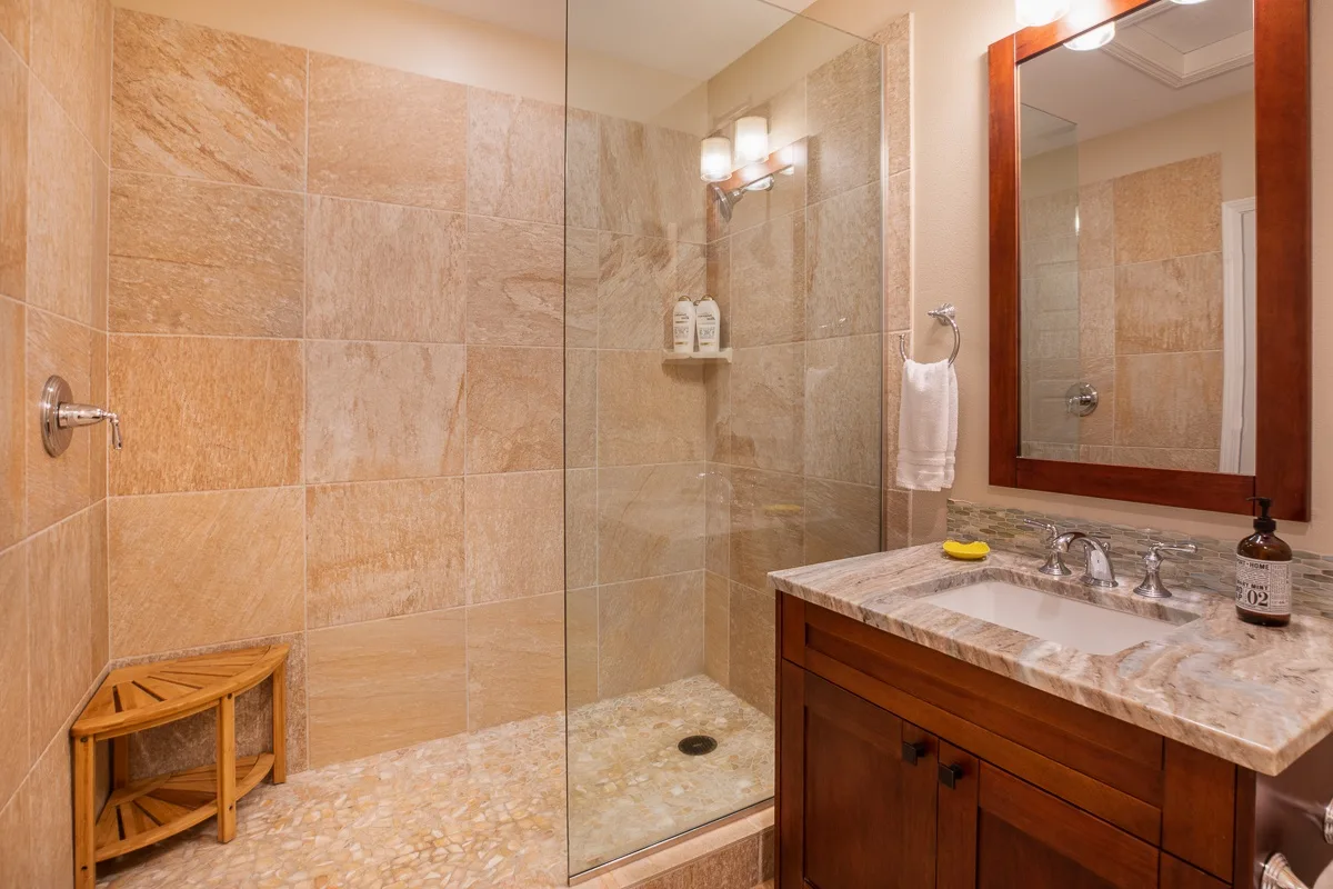 A tiled bathroom with a glass shower and a wooden vanity.