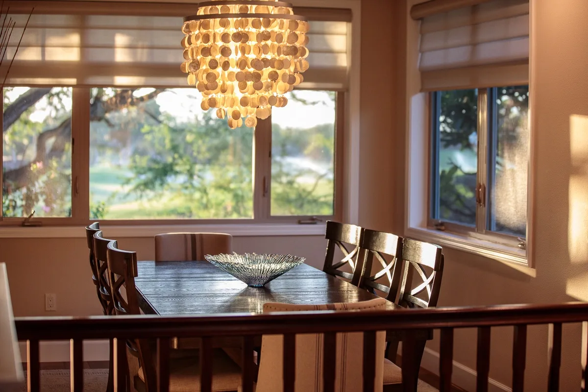 A dining area with a wooden table and a hanging chandelier beside large windows.