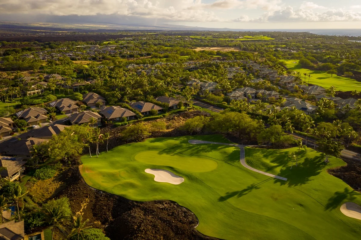 An aerial view of a golf course green with a sand bunker and nearby homes.