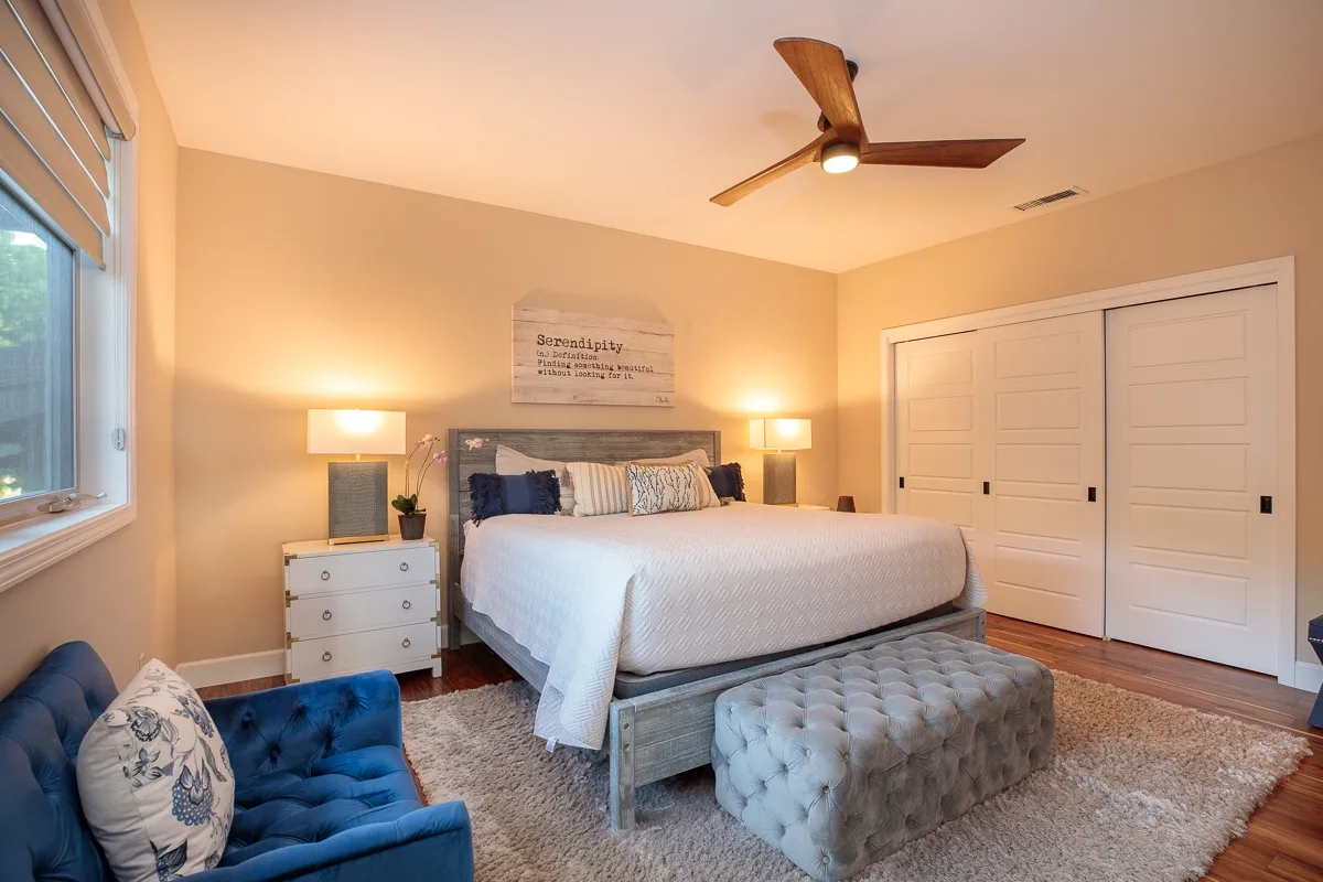 A bedroom with a neatly made bed, bedside lamps, and a tufted bench.