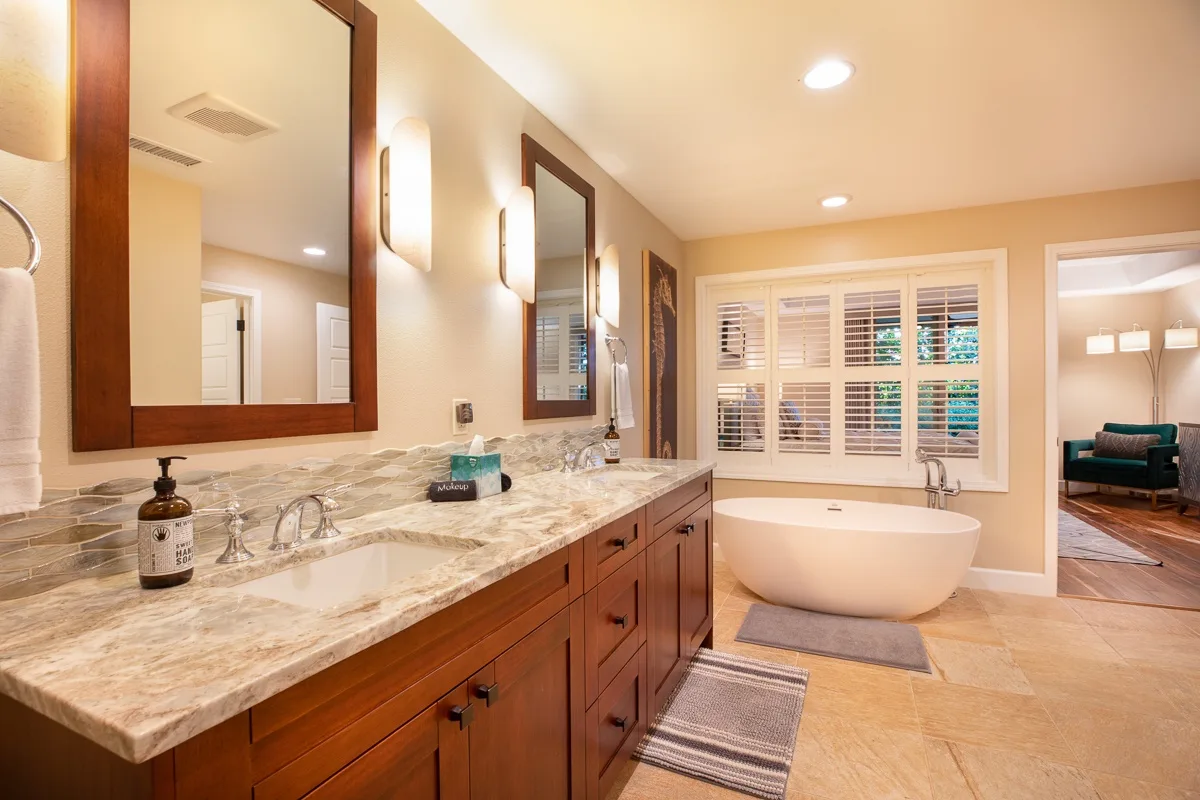 A bathroom vanity and bathtub sit beneath windows with white shutters.