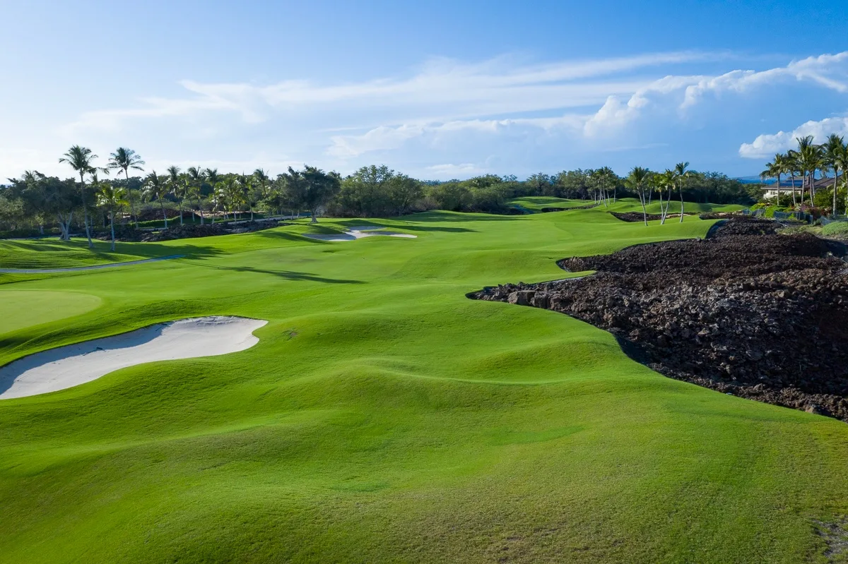 A golf course stretches across rolling green fairways beside a rocky shoreline.