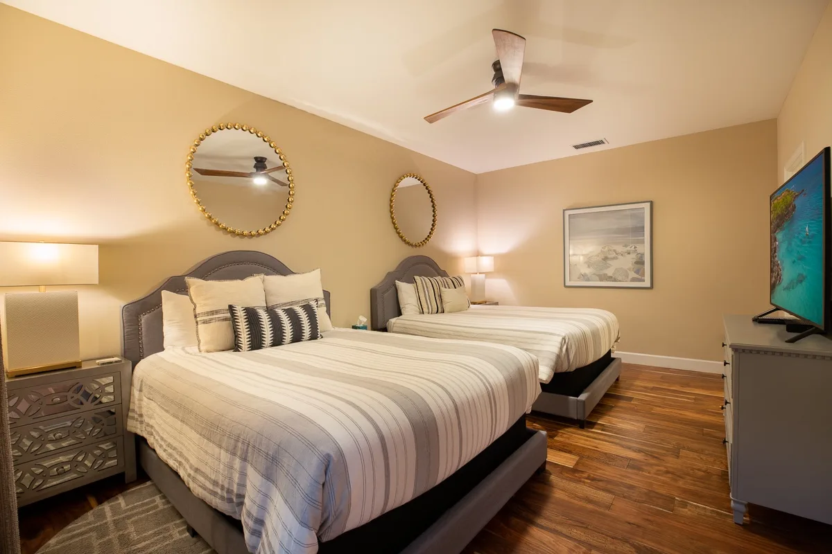 A bedroom with two beds, bedside tables, and a ceiling fan.