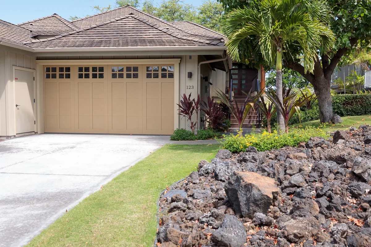 A house exterior with a garage, driveway, lawn, and landscaped rock garden.