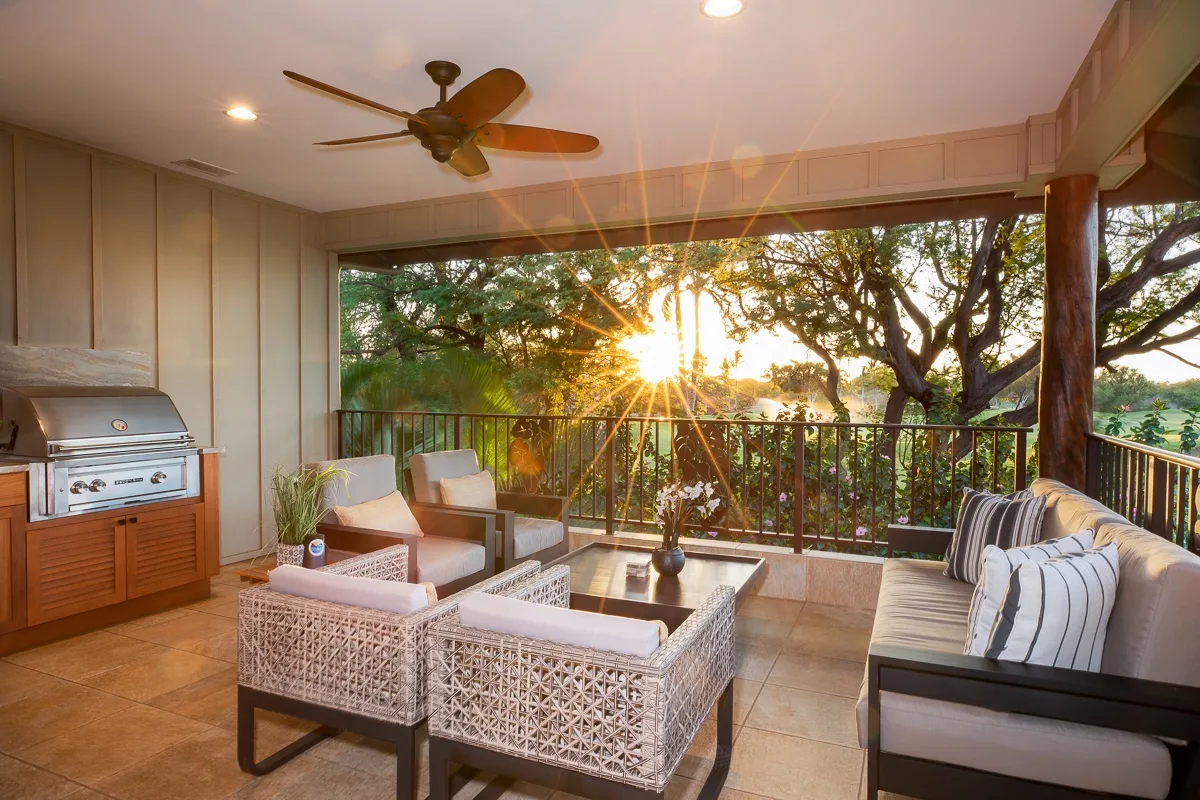 A covered patio with cushioned seating overlooks trees in the evening light.