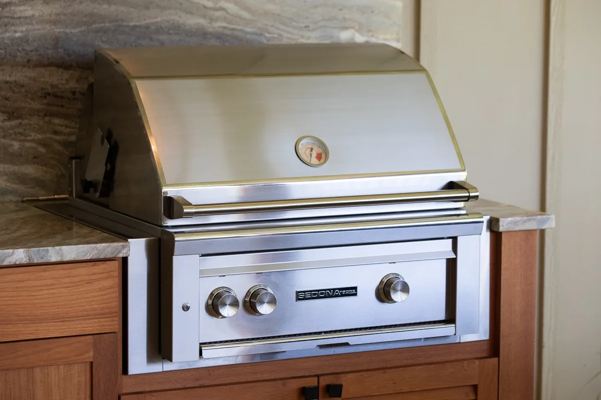 A stainless steel barbecue grill is built into wooden outdoor kitchen cabinetry.