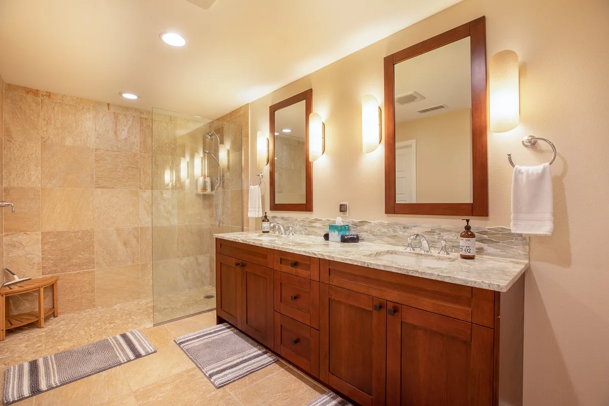 A spacious bathroom with a long wooden vanity, mirrors, and a tiled shower area.