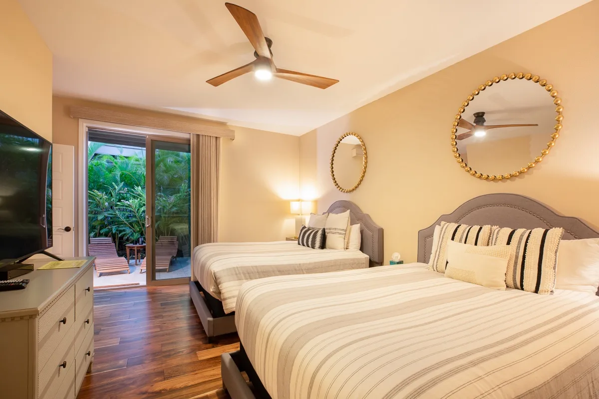 A bedroom with two beds, striped bedding, and a sliding glass door opening to greenery.