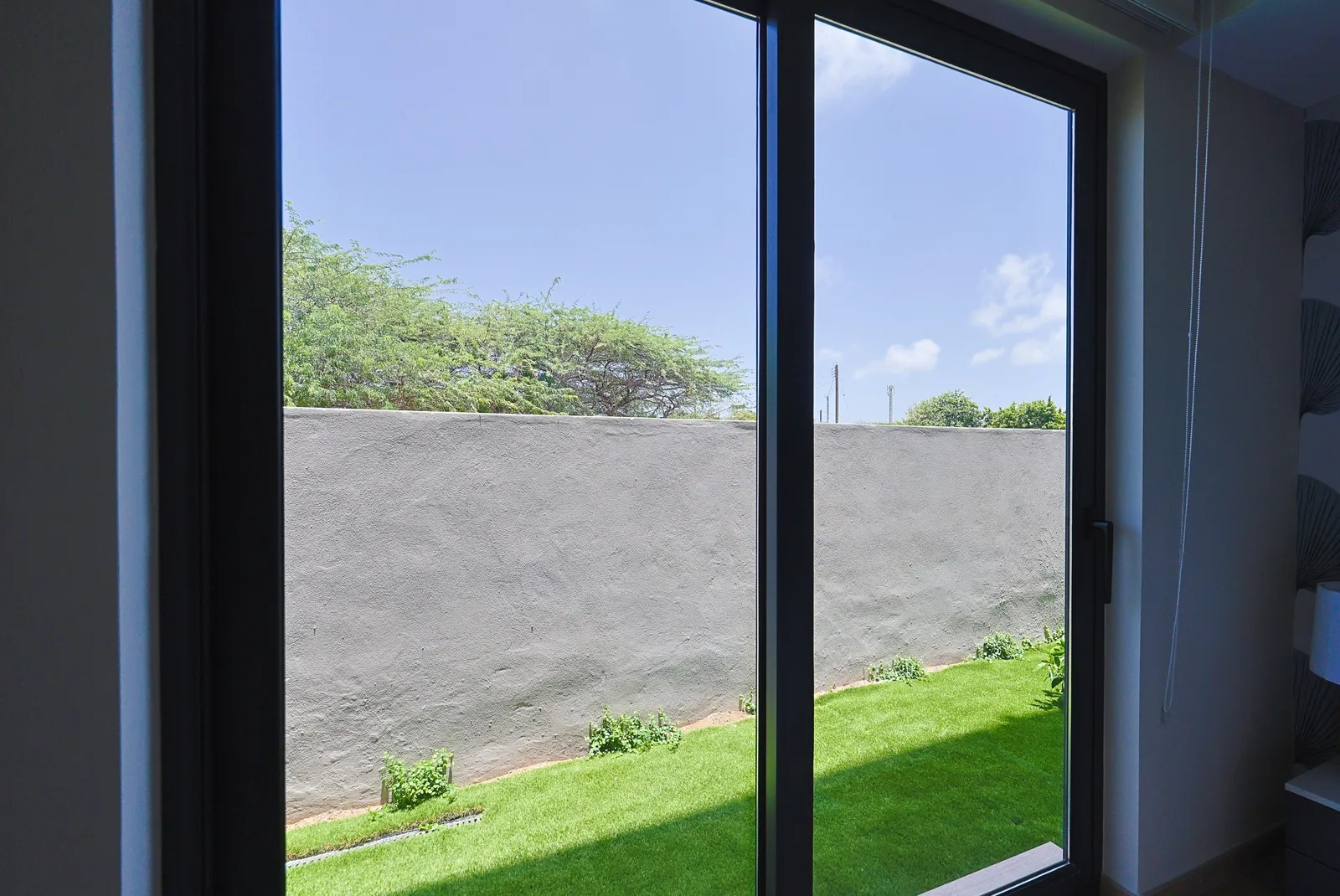 Bright natural light fills your room through large glass doors opening to a private outdoor space with fresh green lawn and clear blue skies above.