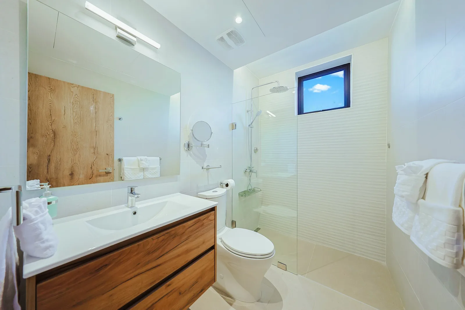 Your bathroom features a modern glass shower, warm wood accents, and fresh white towels awaiting your arrival. Natural light streams in, creating a calm, spa-like retreat.