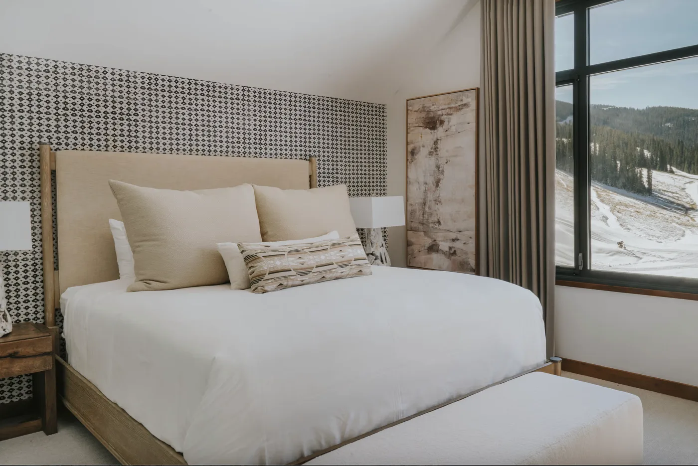 A bedroom with a neatly made bed beside a large window overlooking a snowy landscape.