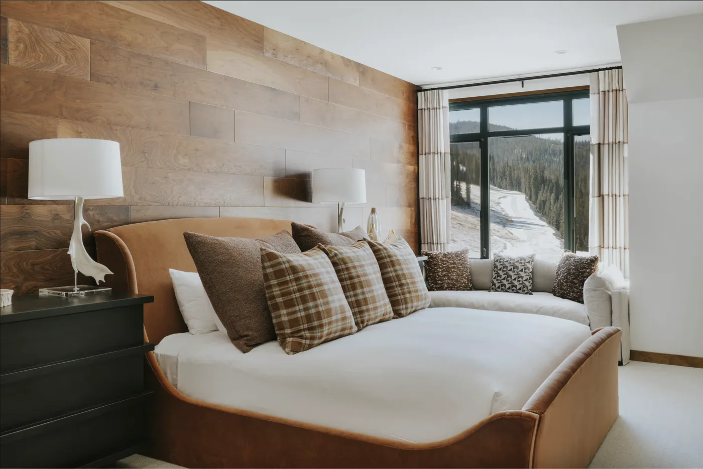 A bedroom with a large bed facing a glass door and snowy scenery.