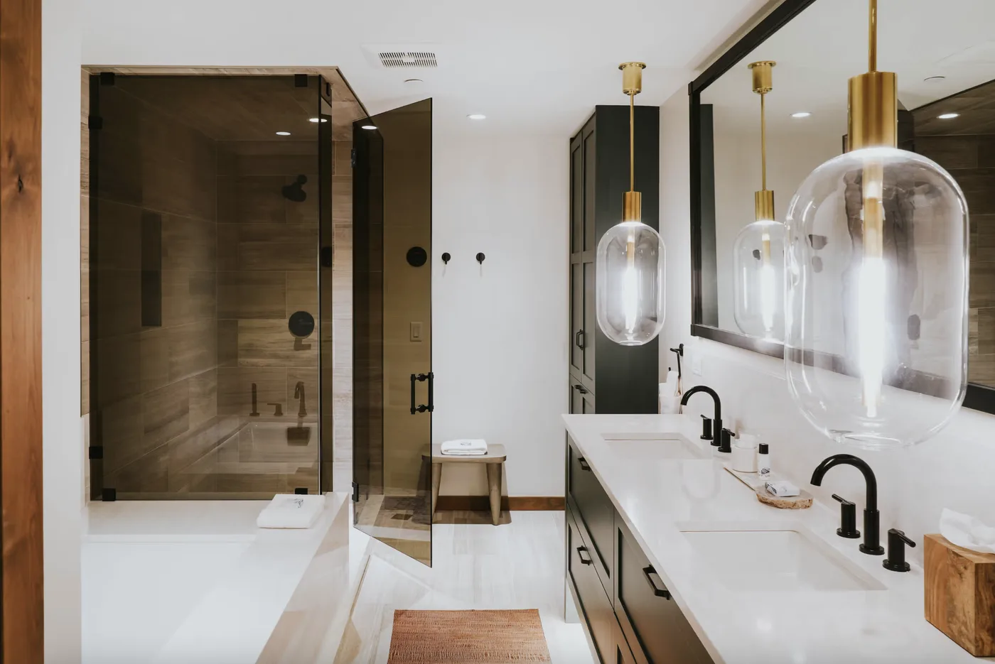 A modern bathroom with a glass shower, bathtub, and a long vanity.